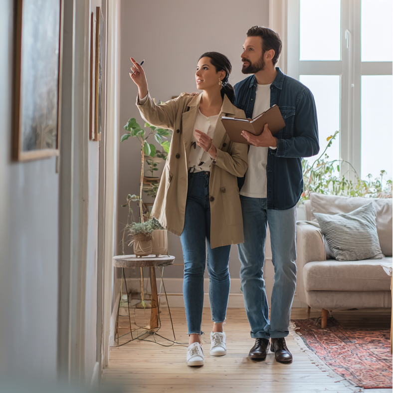 a couple walking through a house; a woman is pointing and both the man and woman are looking in the direction she is pointing.